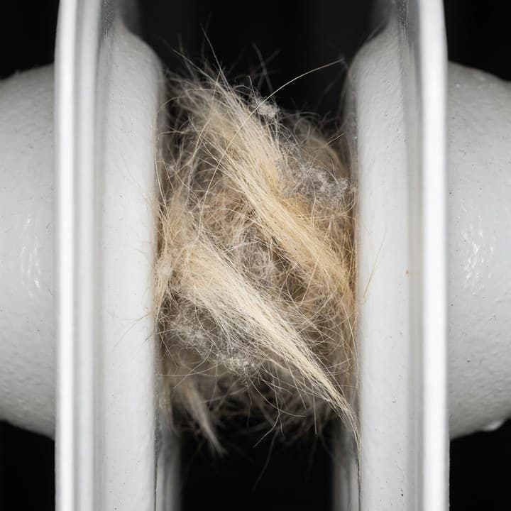Makro detail — chumáč zvieracích chlpov medzi rebrami radiátora